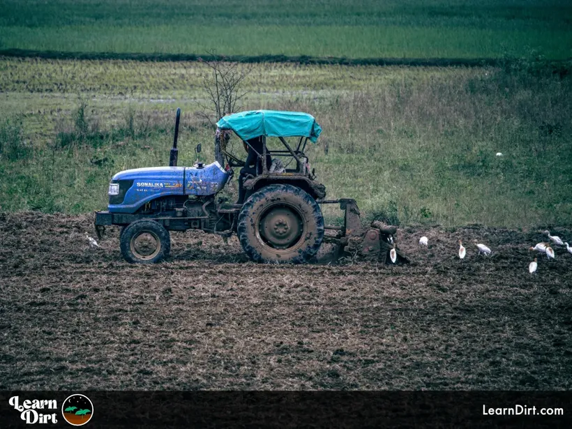 plowing field with blue tractor white birds following behind to pick out worms